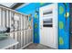 Exterior of a building featuring an outdoor shower with metal storage shelves, and a vivid blue wall with bright green leaf designs at 6417 Klaus Ct, Port Charlotte, FL 33981