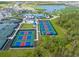 Aerial view of tennis courts, pickleball courts, and community pool with lake and homes in the background at 12470 Wellen Golf St # 108, Venice, FL 34293