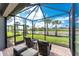 View of the screened-in patio showing outdoor chairs and ottomans with a view of the lawn and lake at 13859 Vadini St, Venice, FL 34293