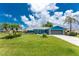 Beautiful blue home featuring a lush lawn, mature palm trees, stone accents, and tidy landscaping at 23 Bunker Cir, Rotonda West, FL 33947