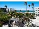 Tropical courtyard with shaded lounge areas, dining sets, lush palm trees, and ocean views in the background at 5700 Gulf Shores Dr # B-137, Boca Grande, FL 33921