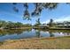 Scenic lake view with lush trees reflecting in the clear water under a bright blue sky at 232 Southampton Ln # 259, Venice, FL 34293