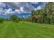 Expansive backyard with a lush green lawn, mature trees, and a clear blue sky with scattered clouds at 13051 Creekside Ln, Port Charlotte, FL 33953