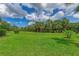 Well-manicured backyard featuring lush green grass, mature trees, and a clear blue sky with fluffy clouds at 13051 Creekside Ln, Port Charlotte, FL 33953