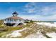 Charming beach house on stilts with stairs leading to a sandy shore, green vegetation, and clear blue sky at 15610 Staunton Cir, Port Charlotte, FL 33981