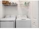 Well-lit laundry room with white washer and dryer, overhead shelving, and cleaning supplies at 12550 Galapagos Ct # 104, Venice, FL 34293