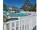 Community pool with an attached spa, surrounded by a white fence, shaded tables, and palm trees with tropical landscaping at 1401 S Mccall Rd # 101, Englewood, FL 34223