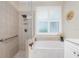 Bright bathroom featuring a tub under a window with plantation shutters and a tiled walk-in shower at 3207 Village Ln, Port Charlotte, FL 33953
