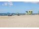 A sunny beach scene with people relaxing under umbrellas and a lifeguard tower in the background at 12470 Wellen Golf St # 107, Venice, FL 34293