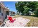 Spacious backyard with a small patio, two red chairs, and mature trees offering shade at 1730 Bluebird Ln, Englewood, FL 34224