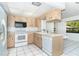 Bright kitchen featuring wood cabinetry, white appliances, and tile flooring with views to backyard at 7059 Quigley St, Englewood, FL 34224