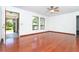 Bright living room featuring hardwood floors, ceiling fan, and large windows with tropical landscaping views at 7059 Quigley St, Englewood, FL 34224