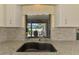 Granite counters and tiled backsplash highlight this kitchen sink with a view of the outdoor pool and lanai at 7218 Darlington St, Englewood, FL 34224