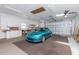 View of a clean garage featuring a turquoise Mazda Miata, overhead lighting, and white storage cabinets at 9457 Heartwellville Ave, Englewood, FL 34224