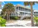 Beach house exterior featuring screened porches and staircase surrounded by lush tropical foliage and mature palm trees at 7500 Palm Island S Dr # 2111, Placida, FL 33946