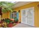 Charming front entrance with a tropical-themed garden, vibrant yellow facade, and white double doors at 401 Sunset Dr, Venice, FL 34285