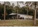 View of white barn with black roof and surrounding grass and woods at 18142 Powerline Rd, Dade City, FL 33523