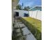 Side yard with a concrete path and overgrown greenery, enclosed by a white fence, next to an AC unit at 9015 Bay Ne St, St Petersburg, FL 33702