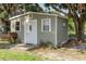 Exterior view of the shed with a white door and window, complemented by lush plants and a large tree at 2638 E Knights Griffin Rd Rd, Plant City, FL 33565
