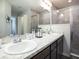 Bright bathroom featuring double sinks, granite countertops, dark wood cabinets, and a walk-in shower with glass doors at 7076 162Nd E Pl, Parrish, FL 34219