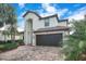 Front view of a two-story home with a terracotta tile roof, black two-car garage, and a brick paver driveway at 6914 Quiet Creek Dr, Bradenton, FL 34212