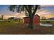 View of the red outbuilding, concrete pad near a mature tree and spacious yard during sunset at 3715 Fortner Rd, Plant City, FL 33567