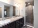Modern bathroom featuring dual sinks, a large mirror, a walk-in shower and dark cabinets at 35402 Coventry Fields Loop, Zephyrhills, FL 33541
