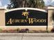 Entrance sign for Auburn Woods community featuring a black background, gold lettering and a palm tree design at 218 Auburn Woods Cir, Venice, FL 34292