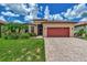 Tan house with red garage door, lush landscaping, and paved driveway at 20193 Pezzana Dr, Venice, FL 34292