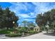 Community entrance with a guard house, manicured landscaping, mature trees, and a decorative lamp post at 217 Carriage House Ln # 217, Nokomis, FL 34275