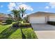 Exterior view of a light beige villa with a two-car garage, lush landscaping, and palm trees at 3897 Fairway Dr, North Port, FL 34287