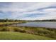 Scenic lake view with lush green grass and neighborhood residences lining the bank beneath a partly cloudy sky at 5584 Cantucci St, Nokomis, FL 34275