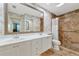 Bright bathroom featuring dual sinks, white cabinetry, tiled shower, and decorative wallpaper at 5856 Helicon Pl, Sarasota, FL 34238