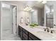 Bright main bathroom with double sinks, granite countertops, dark cabinetry, and a view of the walk in closet at 13864 Posada St, Venice, FL 34293