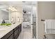 Bright main bathroom with double sinks, granite countertops, dark cabinetry, a glass shower, and a view of the main bedroom at 13864 Posada St, Venice, FL 34293