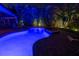 Backyard with a vibrant blue-lit pool and jacuzzi surrounded by mature tropical landscaping for ultimate privacy at 828 The Rialto, Venice, FL 34285