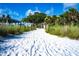 Sandy path leads to Siesta Key beach, framed by lush vegetation and wooden posts against a blue sky at 110 Vista Hermosa Cir # 102B, Sarasota, FL 34242