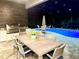 Outdoor kitchen and dining space overlooking a sparkling pool with elegant lighting for evening entertaining at 19836 Bridgetown Loop, Venice, FL 34293