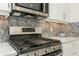 Close-up of the stainless steel gas range and microwave with granite countertops and mosaic backsplash at 5665 Piccolo St, Nokomis, FL 34275