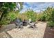 Backyard seating area with four chairs and a center table surrounded by lush greenery and landscaping at 1700 Manasota Beach Rd, Englewood, FL 34223