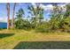 Backyard with a grassy area partially covered by shadow from trees and a blue building in the distance at 3716 Dunbar Rd, Venice, FL 34293