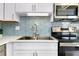 Close-up of kitchen sink and stove with modern backsplash and white countertops at 6415 Midnight Pass Rd # 909, Sarasota, FL 34242