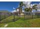 Backyard with a well-maintained lawn enclosed by a wrought iron fence and mature palm trees at 8969 Mondial Ct, Venice, FL 34293