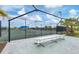 Tennis court with an awning, fencing, and a bench area, with lush greenery and landscaping around the perimeter at 9916 Bright Water Dr, Englewood, FL 34223