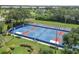 Aerial view of blue and red tennis courts with stadium seating, surrounded by manicured lawns and trees at 454 Cerromar Rd # 174, Venice, FL 34293