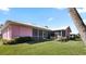 View of the pink home exterior showcasing the screened-in patio, lush lawn, and well-maintained landscaping under a blue sky at 111 2Nd St, Nokomis, FL 34275