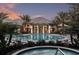 An elegant clubhouse with a large pool and spa, surrounded by palm trees and landscaped grounds at dusk at 12679 Sagewood Dr, Venice, FL 34293