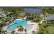 Aerial view of a vibrant community pool featuring a slide, palm trees, and a splash pad near a scenic lake at 12679 Sagewood Dr, Venice, FL 34293