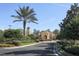 Serene drive-up view of the community clubhouse with lush landscaping, palm trees, and Mediterranean architecture at 174 Treviso Ct, North Venice, FL 34275