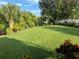 Expansive backyard featuring lush green lawn, tropical foliage and mature trees under a bright blue sky at 213 Bayside Ct, Nokomis, FL 34275